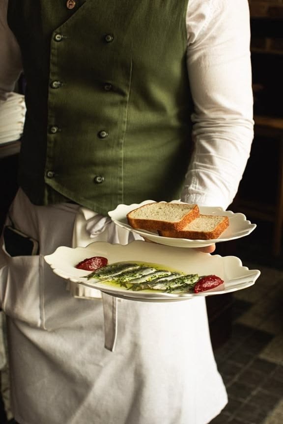 Service bringt Vorspeisenteller mit fein angerichtetem Fisch und Brot an den Tisch