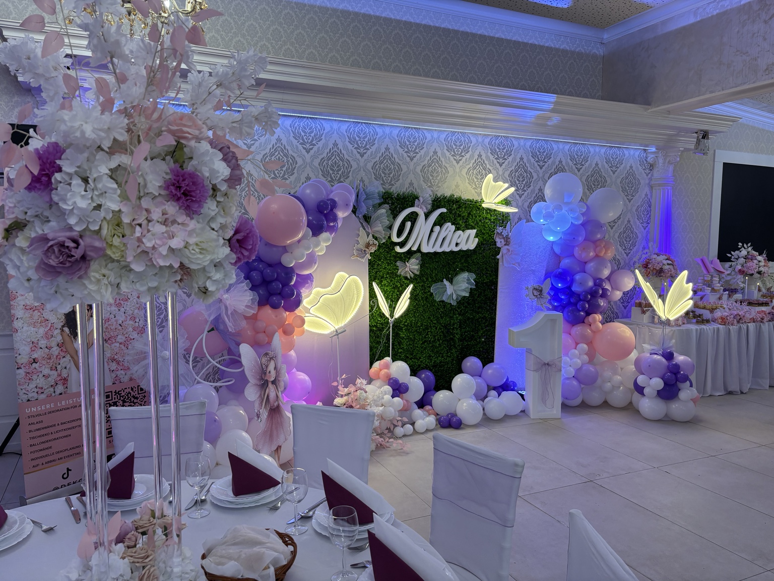 Detailansicht der Schmetterlings-Dekoration mit Blumenarrangement, Ballongirlande und festlich gedeckten Tischen