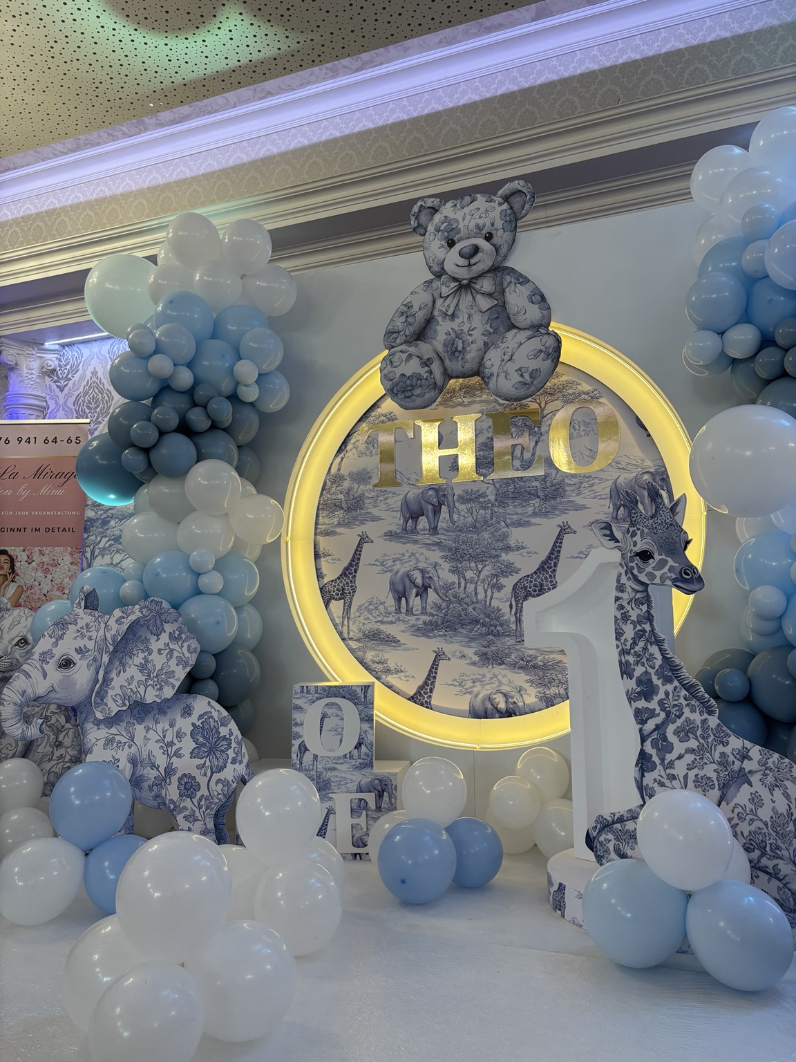 Detail der Safari-Rundwand mit beleuchtetem Namen, Tierfiguren und blau-weißen Ballongirlanden