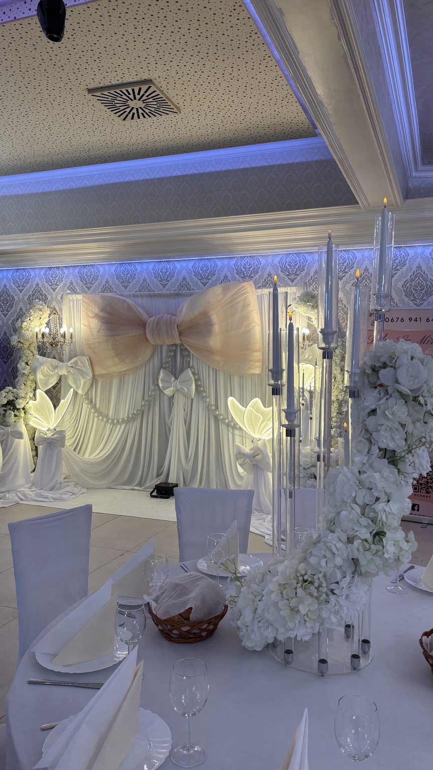 Elegante Tischdekoration vor weißer Schleifenkulisse mit hohen Kerzenleuchtern und Blumenarrangements