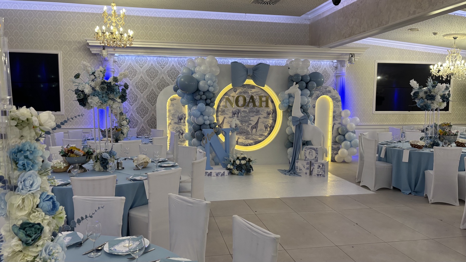 Großer Festsaal für eine Babyfeier in Blau-Weiß mit Karussell-Kulisse, Ballongirlanden und edlen Tischdekorationen