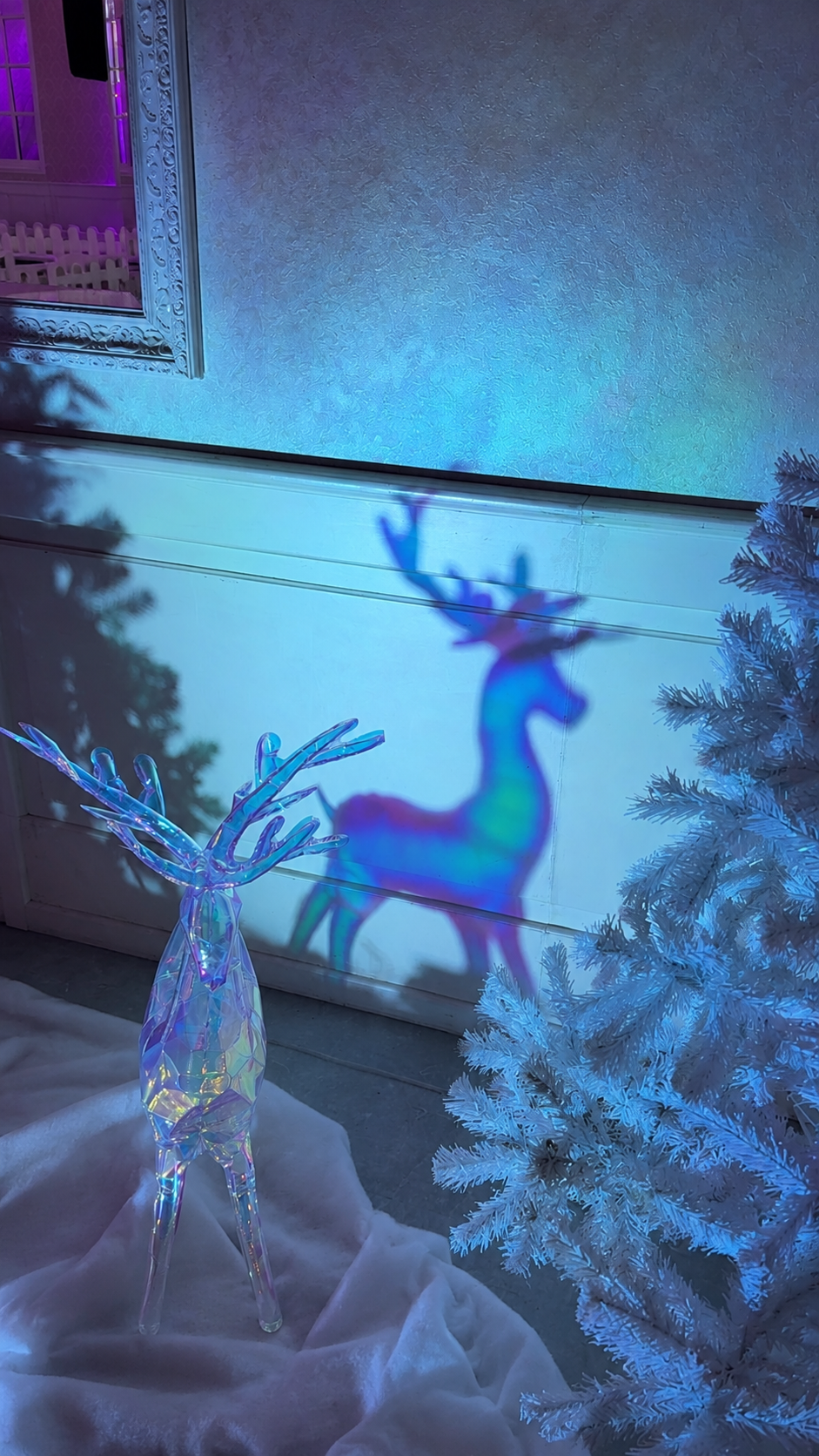 Irisierendes Winterdekor mit gläsernem Rentier, schimmerndem Schattenspiel und weißem Tannenbaum im blauen Licht
