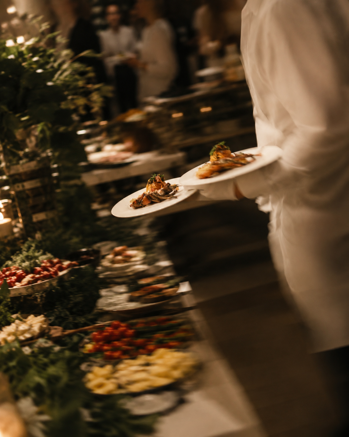 Kellner trägt festlich angerichtete Teller entlang eines dekorierten Buffets im Kerzenschein