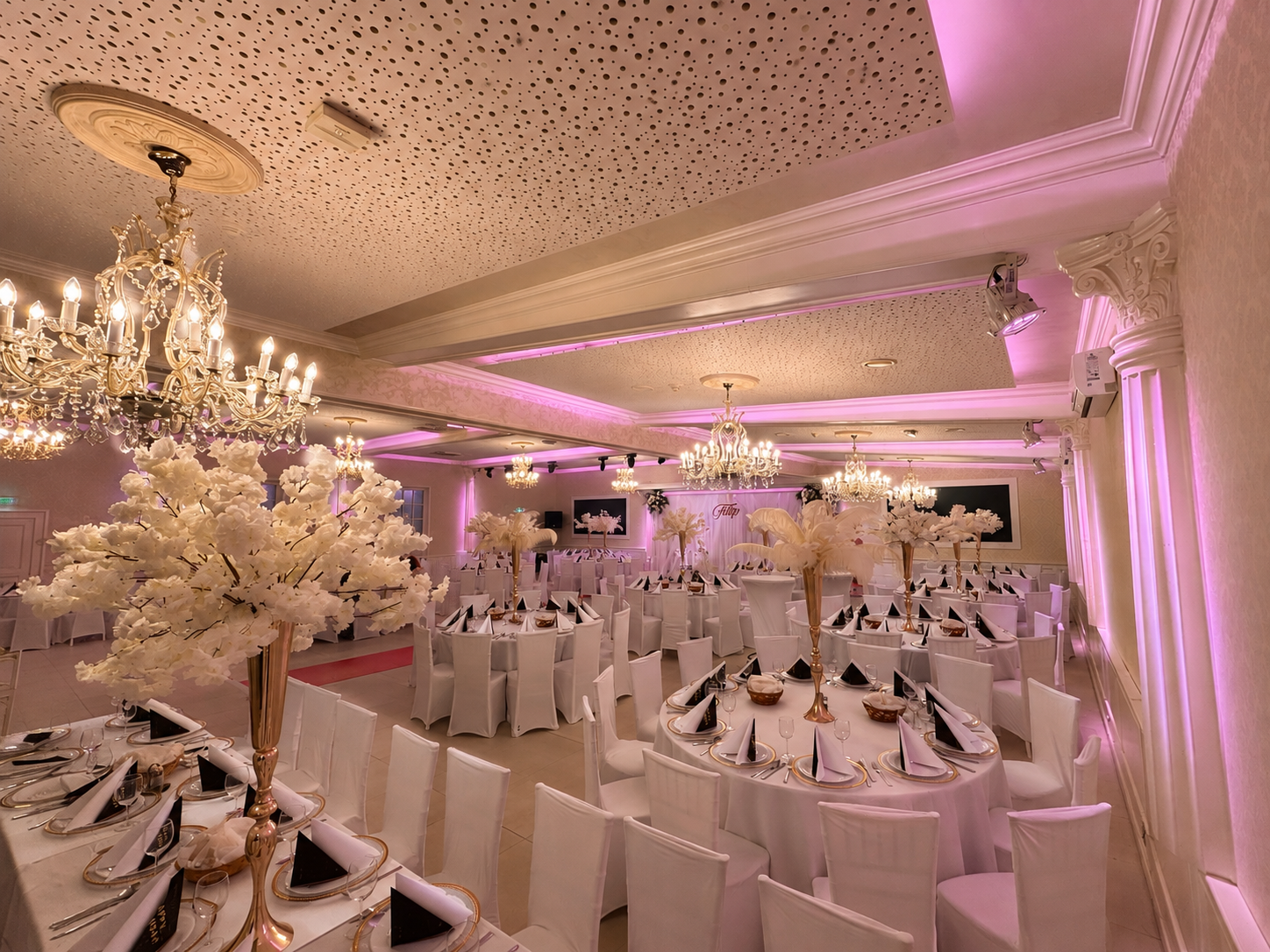 Luxuriöser Festsaal in Rosa und Weiß mit weißen Blütenbäumen, Kronleuchtern und elegant gedeckten Tischen