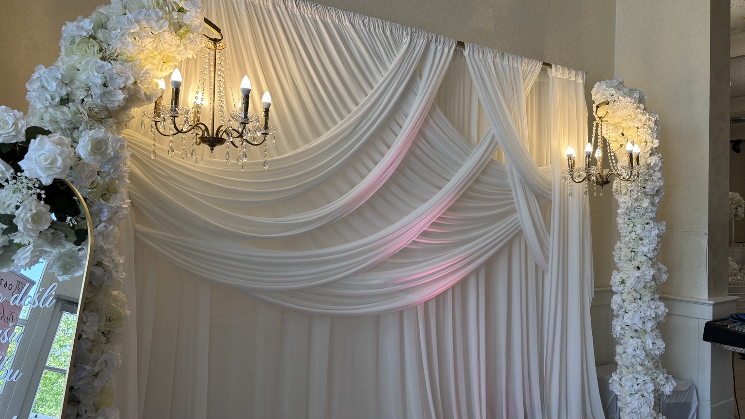 Elegante weiße Stoffkulisse mit Blumenbogen, Kerzenleuchtern und perlengeschmückten Säulen