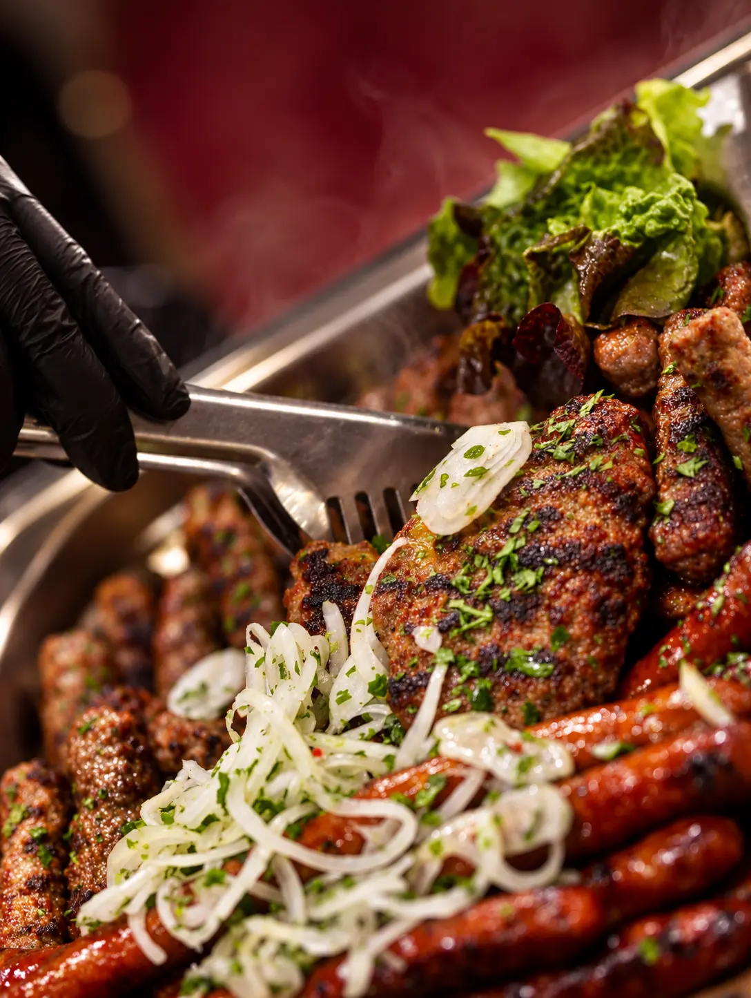 Dampfende Grillplatte mit Fleischspezialitäten und Zwiebeln