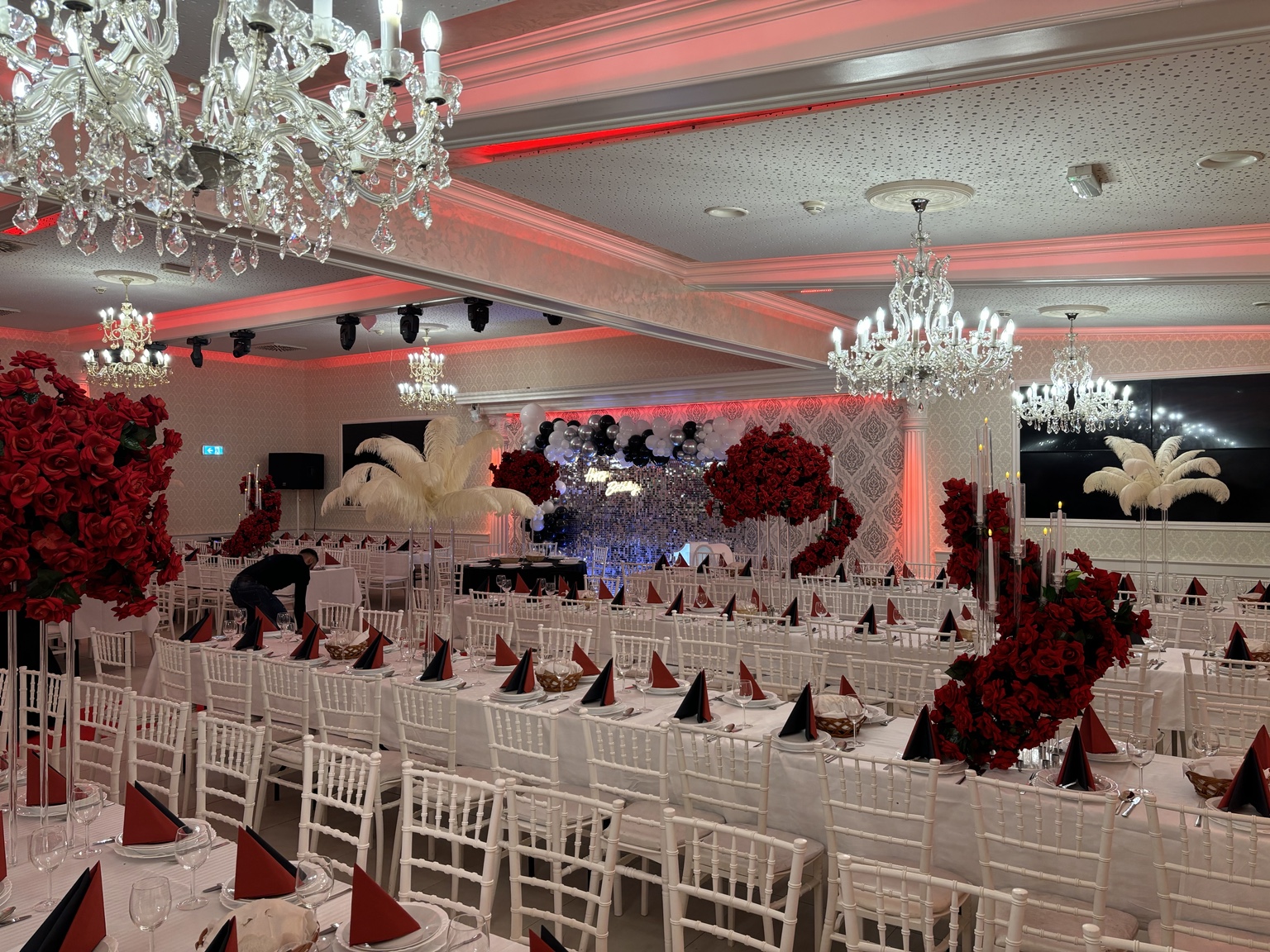 Prunkvoller Festsaal in Schwarz, Weiß und Rot mit großen roten Rosenarrangements, Ballongirlande und Kristallleuchtern