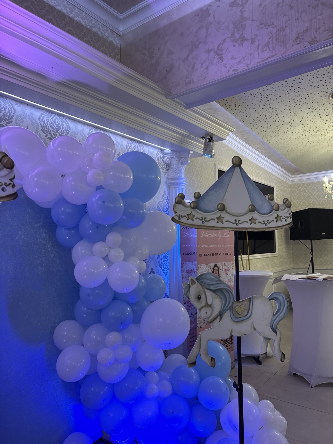 Zauberhafte Kinderfeier-Deko in Hellblau und Weiß mit Karussell-Pferd, Ballongirlande und Namensschriftzug